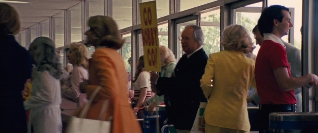 Wide shot frame from Battle of the Sexes — standing, dialogue, suit