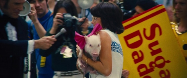 Wide shot frame from Battle of the Sexes — standing, dress, microphone