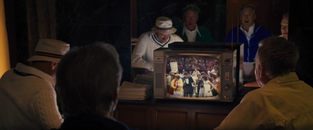 Wide shot frame from Battle of the Sexes — room, dialogue, hat