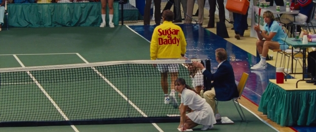 Wide shot frame from Battle of the Sexes — sitting, standing, suit