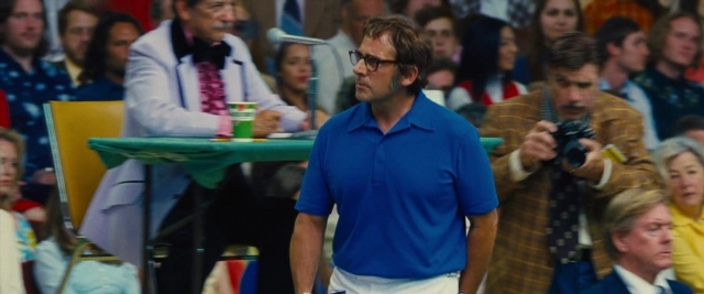 Wide shot frame from Battle of the Sexes — sitting, standing, table