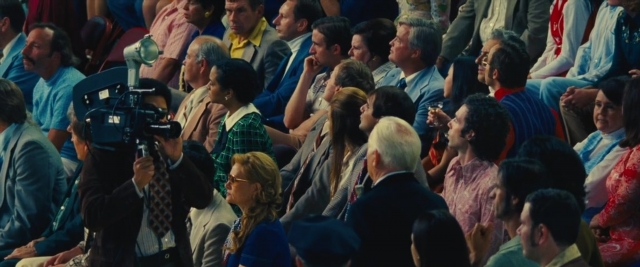 Wide shot frame from Battle of the Sexes — sitting, room, suit