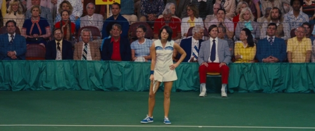 Wide shot frame from Battle of the Sexes — sitting, standing, hand