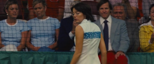 Wide shot frame from Battle of the Sexes — sitting, standing, suit