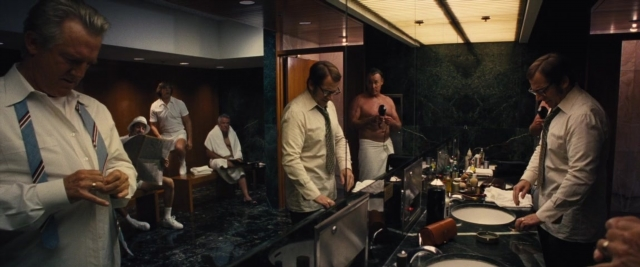 Wide shot frame from Battle of the Sexes — sitting, book, standing