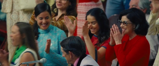 Wide shot frame from Battle of the Sexes — standing, microphone, ring