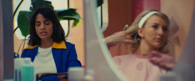 Wide shot frame from Battle of the Sexes — sitting, book, standing