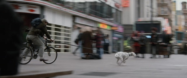 Wide shot frame from 101 Dalmatians — walking, street, hat