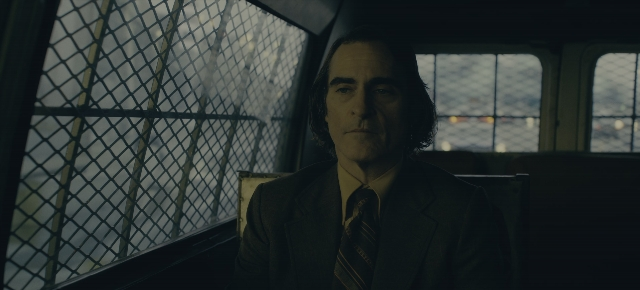 Wide shot frame from Joker: Folie à Deux — sitting, car, suit