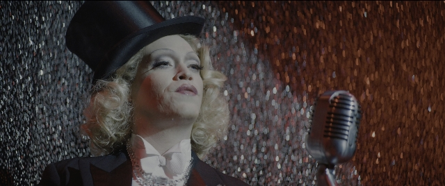 Medium shot frame from Dogman — hat, microphone, face