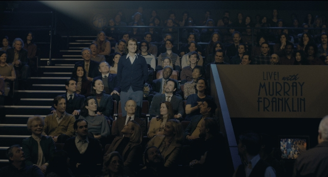 Wide shot frame from Joker — sitting, standing, suit