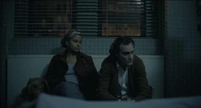 Wide shot frame from Joker — sitting, room, coat