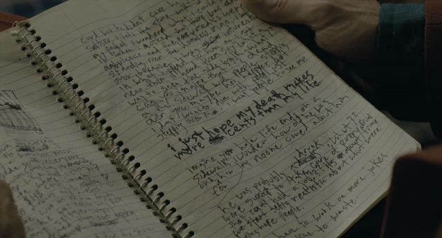 Wide shot frame from Joker — sitting, book, table