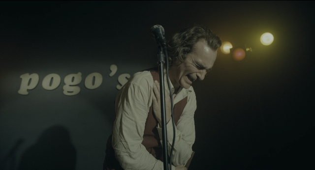 Wide shot frame from Joker — standing, shirt, microphone