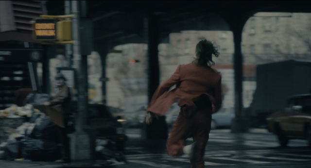 Wide shot frame from Joker — walking, street, car