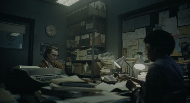 Wide shot frame from Joker — sitting, book, room