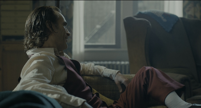 Wide shot frame from Joker — sitting, room, shirt