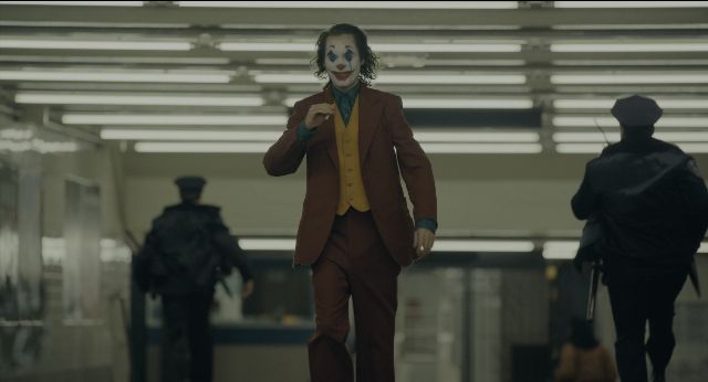 Wide shot frame from Joker — walking, hat, hand