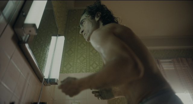 Wide shot frame from Joker — standing, bathroom, face