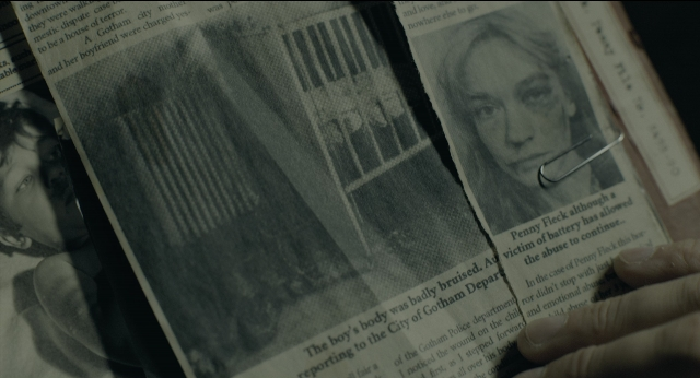 Wide shot frame from Joker — book, face, newspaper