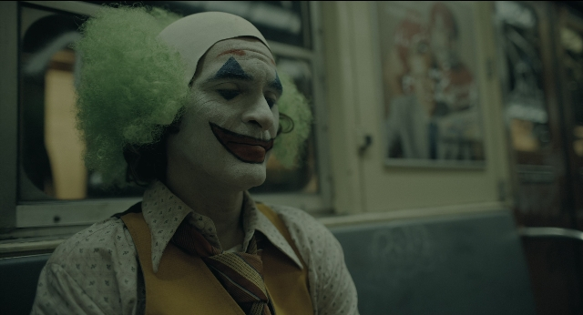 Wide shot frame from Joker — sitting, tie, face