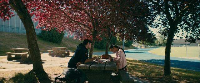 Wide shot frame from To All the Boys I've Loved Before — sitting, book, table