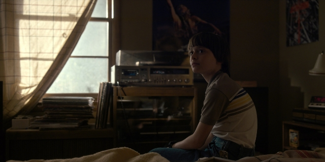 Wide shot frame from Stranger Things — sitting, book, room