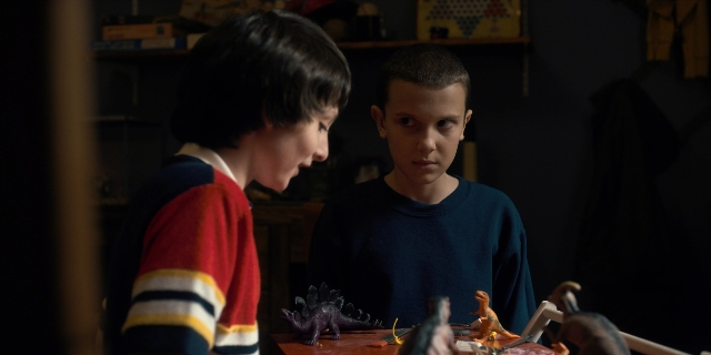 Wide shot frame from Stranger Things — standing, room, table