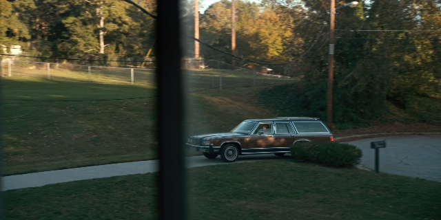 Wide shot frame from Stranger Things — door, street, car