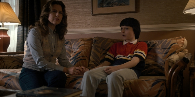 Wide shot frame from Stranger Things — sitting, room, shirt