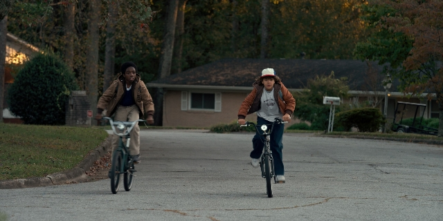 Wide shot frame from Stranger Things — street, hat, bicycle
