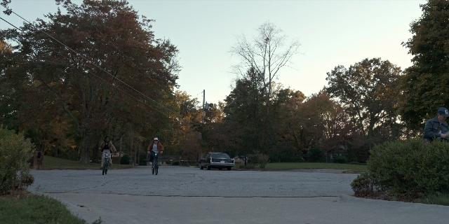 Wide shot frame from Stranger Things — sitting, standing, street