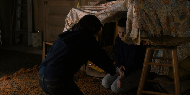 Wide shot frame from Stranger Things — sitting, room, table