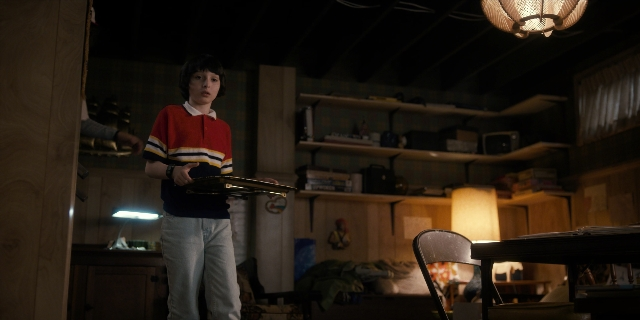 Wide shot frame from Stranger Things — standing, room, table