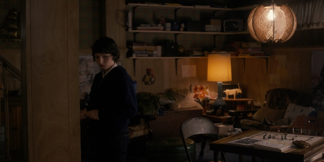 Wide shot frame from Stranger Things — standing, room, table
