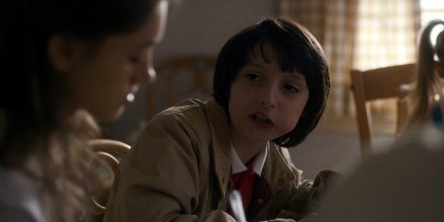 Medium shot frame from Stranger Things — sitting, table, tie