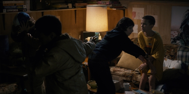 Wide shot frame from Stranger Things — standing, room, hat