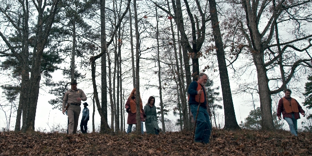 Wide shot frame from Stranger Things — walking, hat, gun