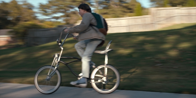 Medium shot frame from Stranger Things — bicycle, backpack, person