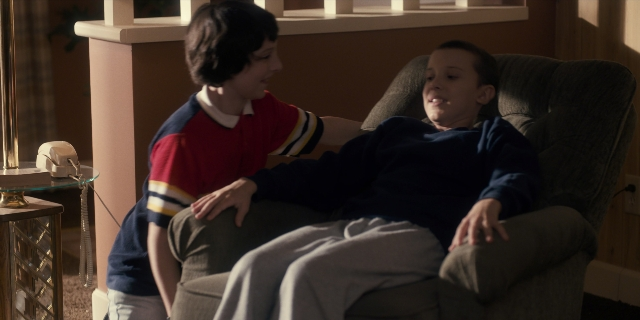 Wide shot frame from Stranger Things — sitting, room, table