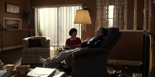 Wide shot frame from Stranger Things — sitting, room, table