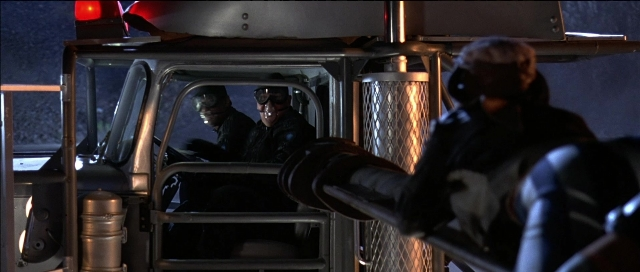 Wide shot frame from Tank Girl — sitting, standing, street