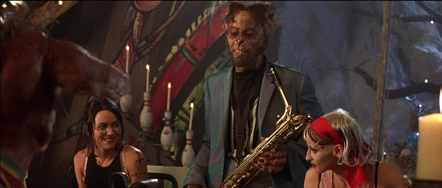 Wide shot frame from Tank Girl — sitting, dialogue, suit