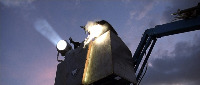 Wide shot frame from Tank Girl — fire, car, smoke