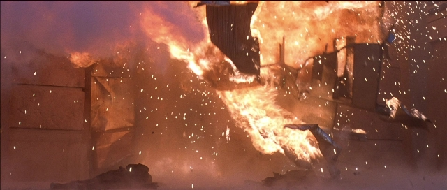 Wide shot frame from Tank Girl — fire, smoke, person