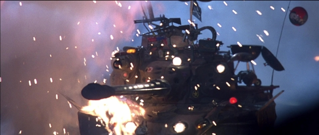 Wide shot frame from Tank Girl — fire, car, night