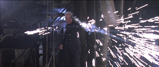 Wide shot frame from Tank Girl — standing, suit, pipe
