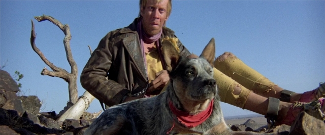 Wide shot frame from Mad Max 2 — sitting, dog, face