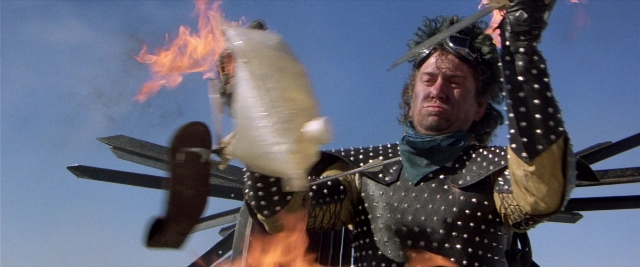 Medium shot frame from Mad Max 2 — standing, hat, hand