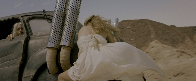Wide shot frame from Mad Max: Fury Road — sitting, car, dress